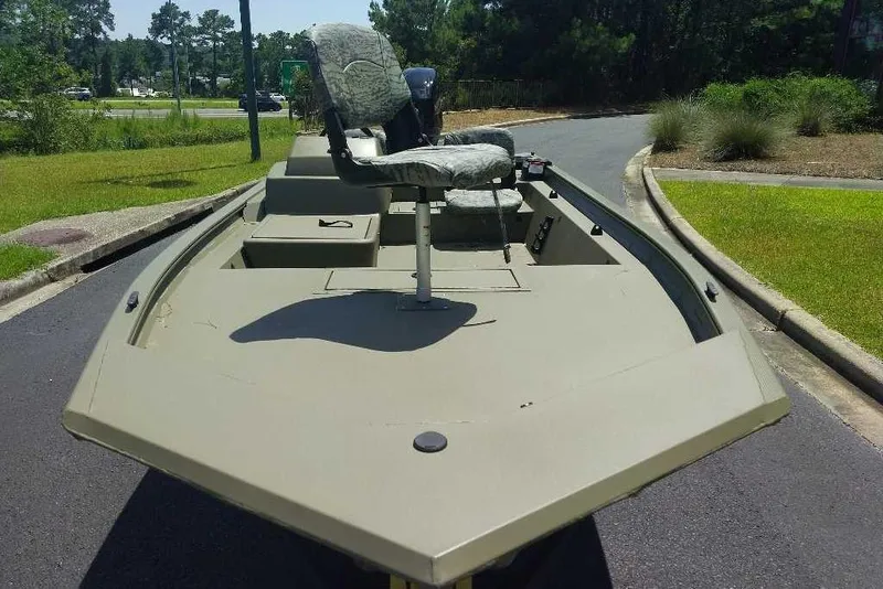 Slide: The Image of 2026 Tracker Grizzly 1754 SC boat with camo seating, parked on a paved road. - 6