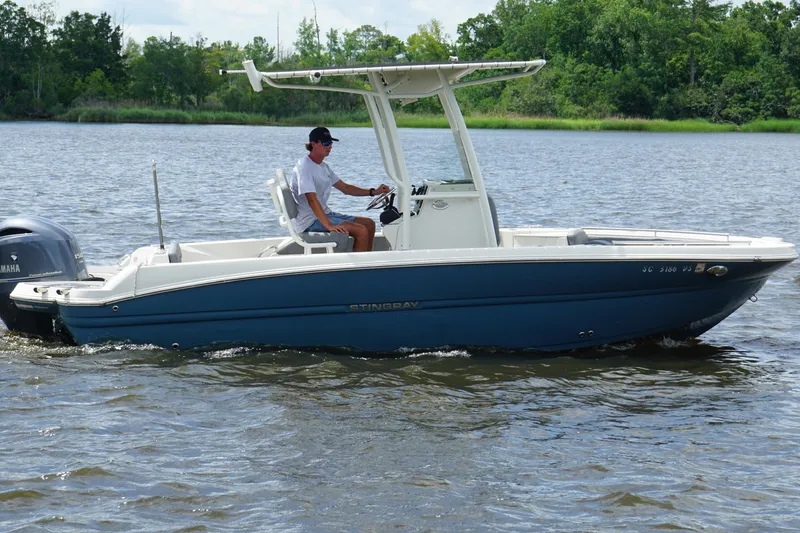 Slide: The Image of 2021 Stingray 216 CC boat cruising on a calm lake with a driver. - 13