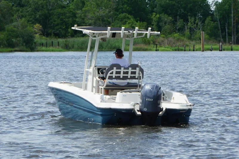 Slide: The Image of 2021 Stingray 216 CC boat cruising on a calm lake with lush greenery in the background. - 14