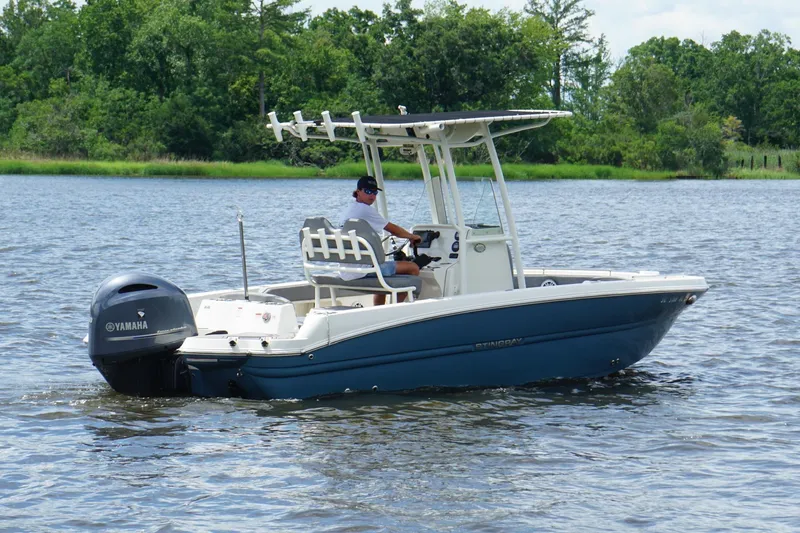 Slide: The Image of 2021 Stingray 216 CC boat cruising on a lake with lush green shoreline. - 3