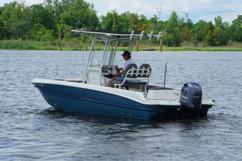 Slide: The Image of 2021 Stingray 216 CC boat cruising on a calm lake with lush greenery. - 4
