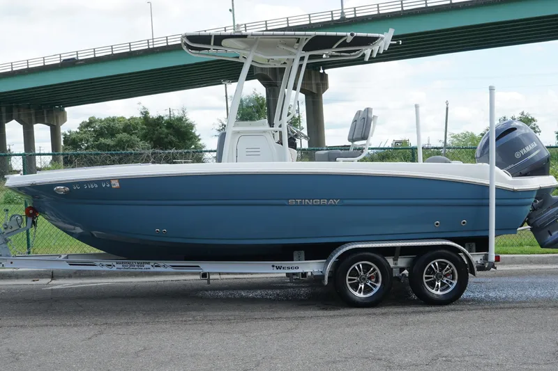 Slide: The Image of 2021 Stingray 216 CC boat on trailer, parked near a bridge, featuring a Yamaha engine. - 5