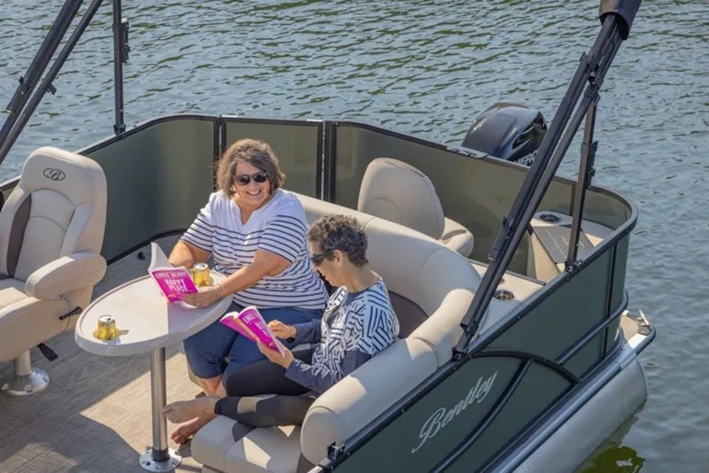 Slide: The Image of Two people relaxing on a 2026 Bentley Pontoons LE 200 CR boat, enjoying drinks and reading. - 4