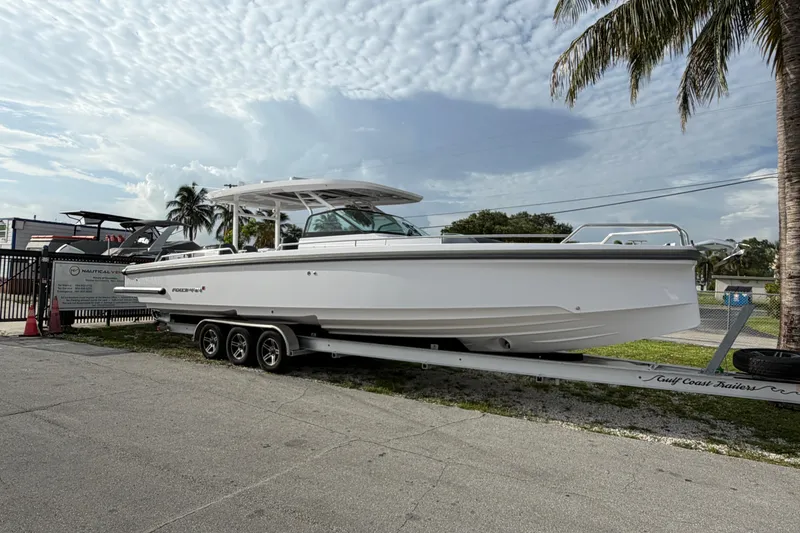 The Image of 2024 Axopar 37 Sun-Top boat on trailer, parked outdoors under cloudy sky. - 0