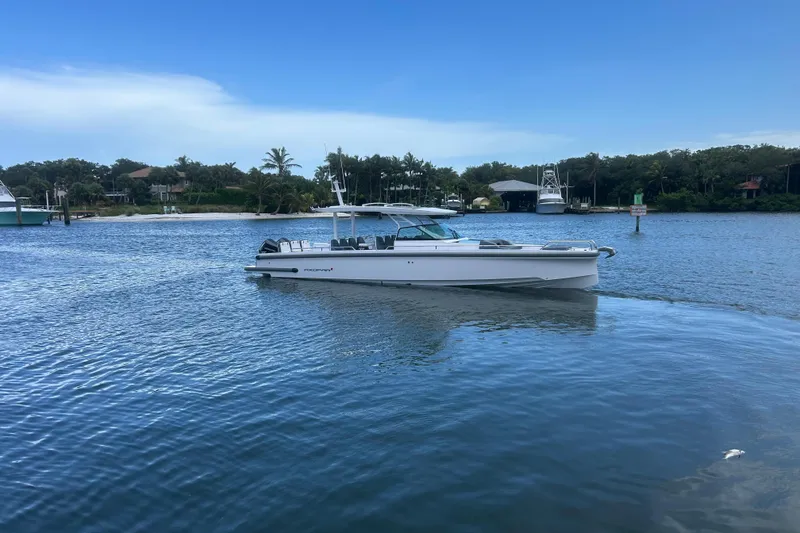 Slide: The Image of 2024 Axopar 37 Sun-Top boat cruising on a serene waterway with lush greenery. - 2
