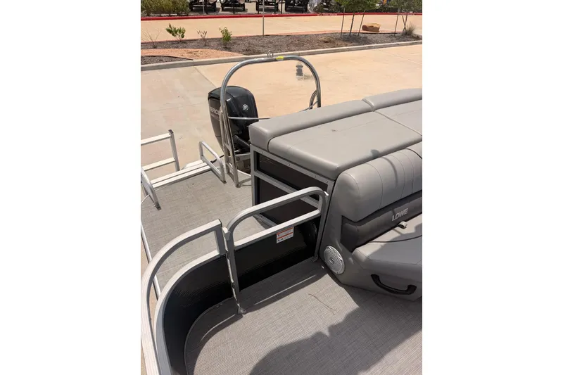 Slide: The Image of 2021 Lowe SS 210 pontoon boat interior with seating and railing, parked on pavement. - 8