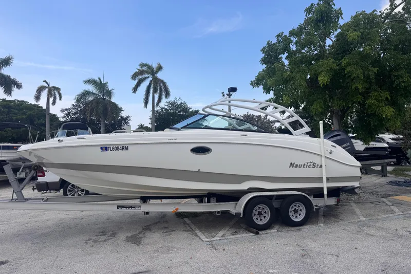 Slide: The Image of 2018 NauticStar 243DC Sport Deck boat on trailer, surrounded by palm trees. - 2