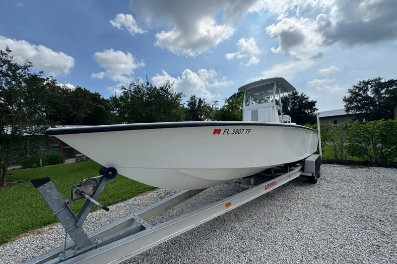 Slide: The Image of White 2022 Rambo 27 boat on trailer, parked on gravel driveway under cloudy sky. - 17