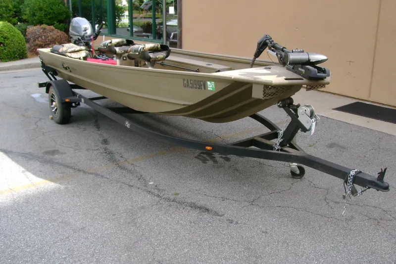 Slide: The Image of 2023 G3 1652 DK boat on trailer, parked outdoors, featuring camouflage seating and motor. - 2