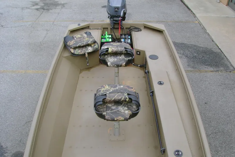 Slide: The Image of 2023 G3 1652 DK boat interior with camouflage seats and motor, parked on pavement. - 8