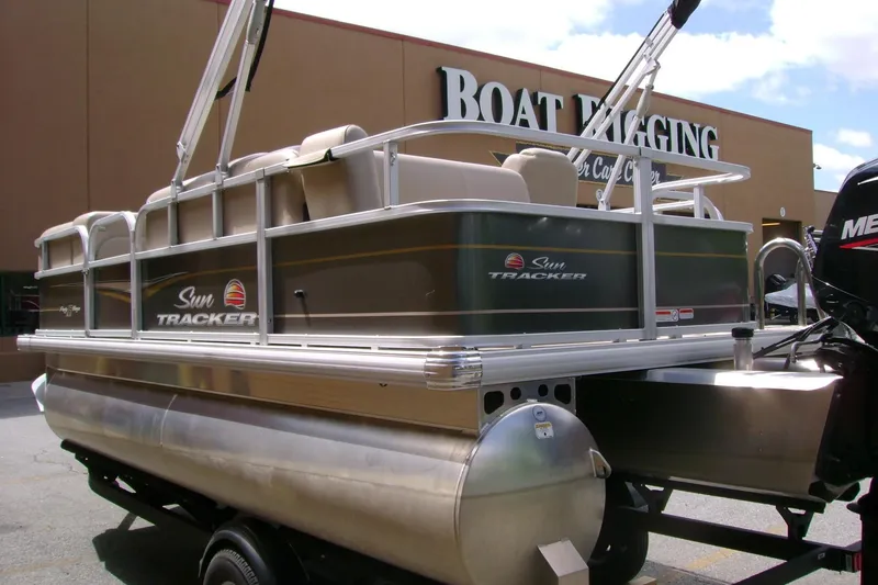 Slide: The Image of 2025 Sun Tracker Party Barge 18 DLX pontoon boat on trailer, parked outside a building. - 13