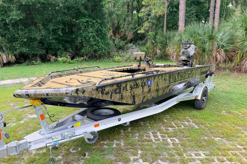 The Image of 2024 Prodigy 1854 boat with camouflage design on a trailer in a wooded area. - 1
