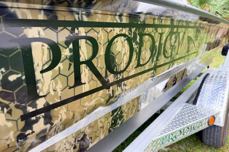 Slide: The Image of 2024 Prodigy 1854 boat with camouflage design and bold lettering on trailer. - 12