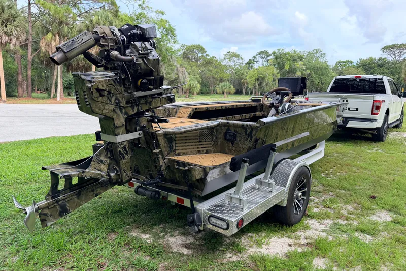 Slide: The Image of 2024 Prodigy 1854 boat on trailer, camo design, parked near white truck in a grassy area. - 4