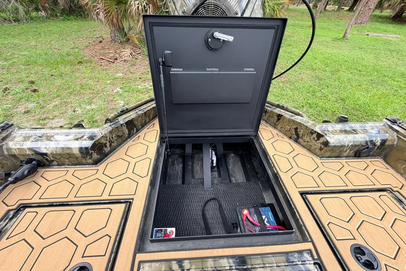 Slide: The Image of Open storage compartment on 2024 Prodigy 1854 boat, featuring camo design and battery setup. - 41
