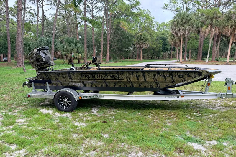 Slide: The Image of 2024 Prodigy 1854 boat on trailer in wooded area, showcasing camouflage design. - 5