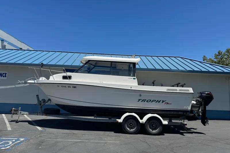 Slide: The Image of 2004 Trophy 2359 WA boat on trailer, parked outdoors under clear blue sky. - 1