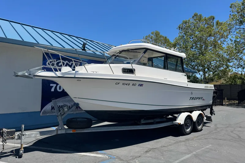 Slide: The Image of 2004 Trophy 2359 WA boat on trailer, parked outdoors under clear blue sky. - 2