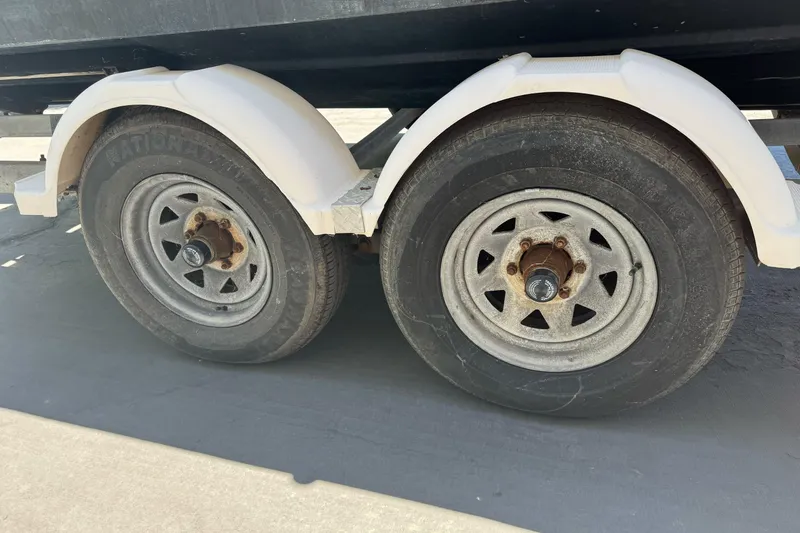 Slide: The Image of Trailer wheels of a 2004 Trophy 2359 WA boat, featuring dual axles and white fenders. - 5