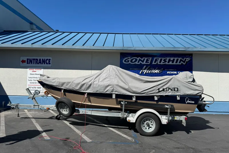 Slide: The Image of 1998 Lund 1700 Pro Sport boat covered on trailer outside marine store. - 2