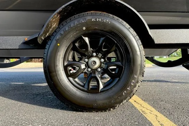 Slide: The Image of 2026 Tracker Pro Guide V-175 WT trailer tire on asphalt, showcasing black alloy wheel design. - 18