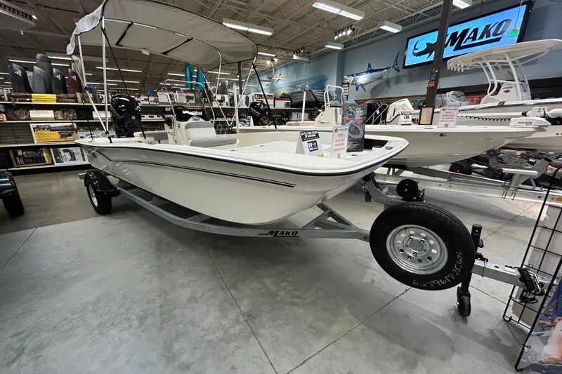 The Image of 2026 Mako Pro Skiff 17 CC boat displayed in a showroom with canopy and trailer. - 0