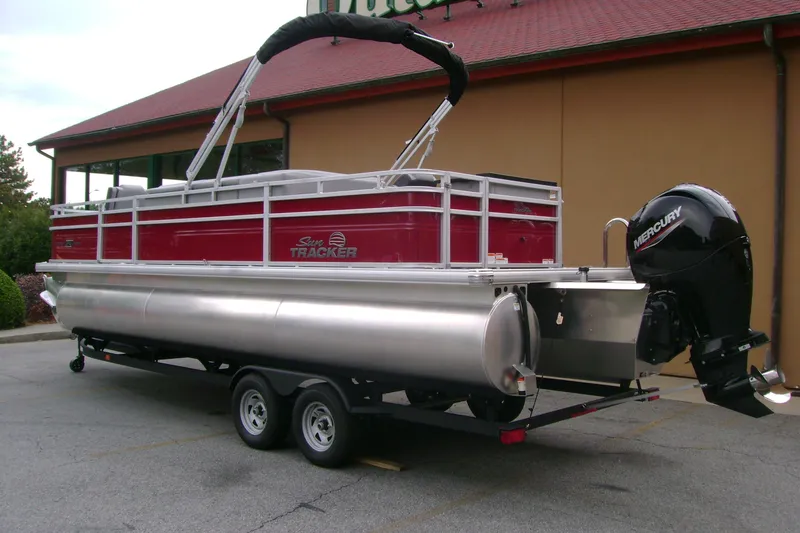 Slide: The Image of 2026 Sun Tracker Sportfish 24 XP3 pontoon boat with Mercury outboard motor, parked outdoors. - 5