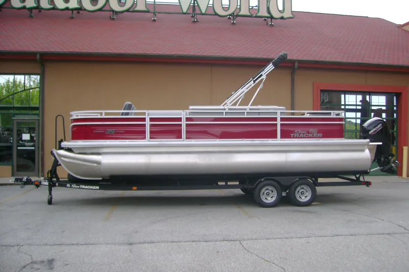 Slide: The Image of 2026 Sun Tracker Sportfish 24 XP3 pontoon boat on trailer outside store. - 99