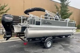 Slide: The Image of 2026 Sun Tracker Bass Buggy 18 DLX pontoon boat on trailer, parked outdoors. - 2