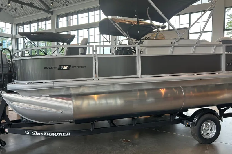 Slide: The Image of 2026 Sun Tracker Bass Buggy 18 DLX pontoon boat displayed indoors on a trailer. - 80