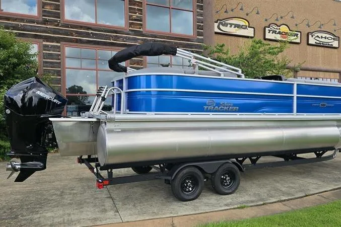 Slide: The Image of 2026 Sun Tracker Party Barge 22 XP3 pontoon boat on trailer, parked outside dealership. - 1