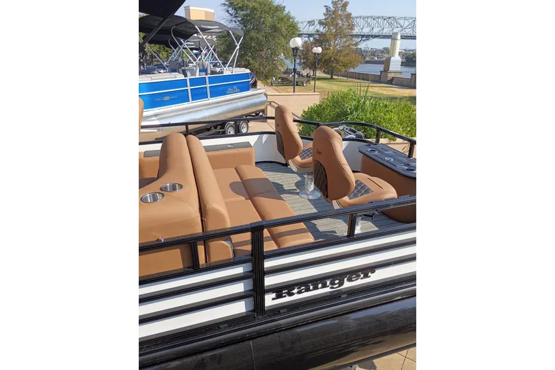 Slide: The Image of 2026 Ranger 223F pontoon boat with tan seating, docked near a scenic riverside bridge. - 7