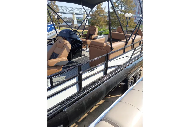 Slide: The Image of 2026 Ranger 223F pontoon boat with tan seating, black railing, and scenic background. - 6