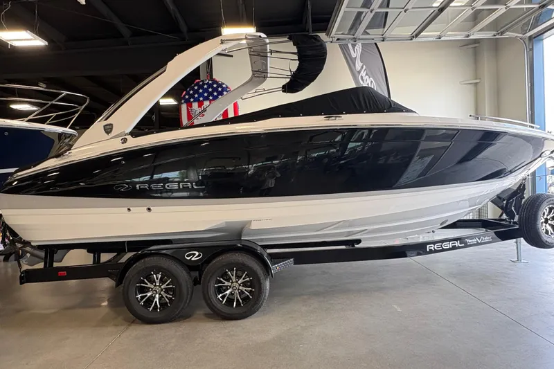 The Image of 2027 Regal LS6 boat on trailer in showroom, featuring sleek black and white design. - 1