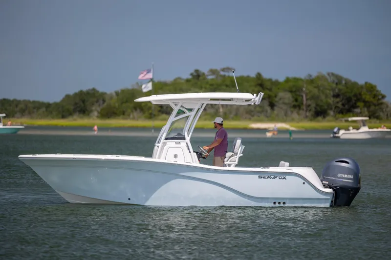 Slide: The Image of 2022 Sea Fox 228 Commander boat cruising on a calm lake with lush green shoreline. - 4