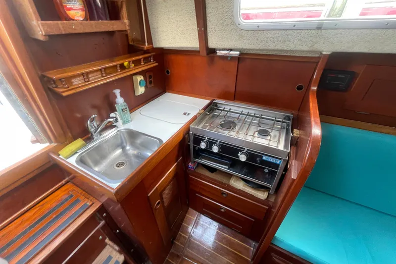 Slide: The Image of Compact galley in 1987 Hallberg-Rassy Monsun 31 sailboat with stove, sink, and wooden cabinetry. - 13