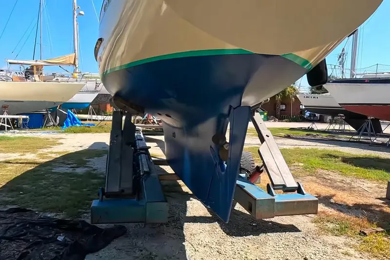 Slide: The Image of Hallberg-Rassy Monsun 31 sailboat from 1987 on a boatyard stand, showcasing its hull. - 28