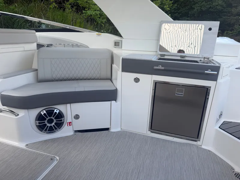 Slide: The Image of The image shows the interior of a 2025 Sea Ray SLX 350 boat. There's a gray bench seat, built-in grill, and refrigerator. The floor is covered with light carpeting. - 21