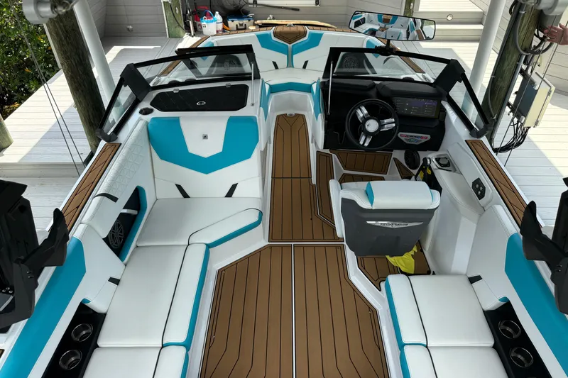 Slide: The Image of 2024 Nautique Super Air Nautique GS20 boat interior with white and blue seating, brown flooring. - 12