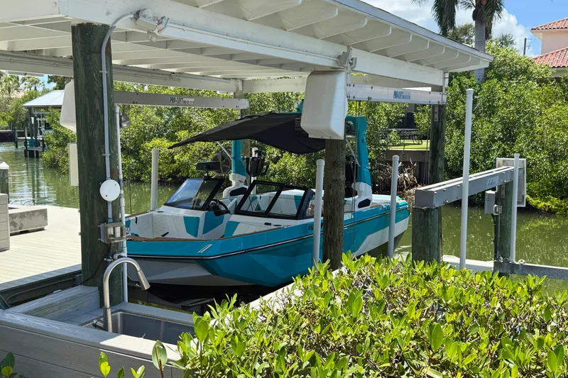 Slide: The Image of 2024 Nautique Super Air Nautique GS20 boat docked under a covered lift in a scenic marina. - 37