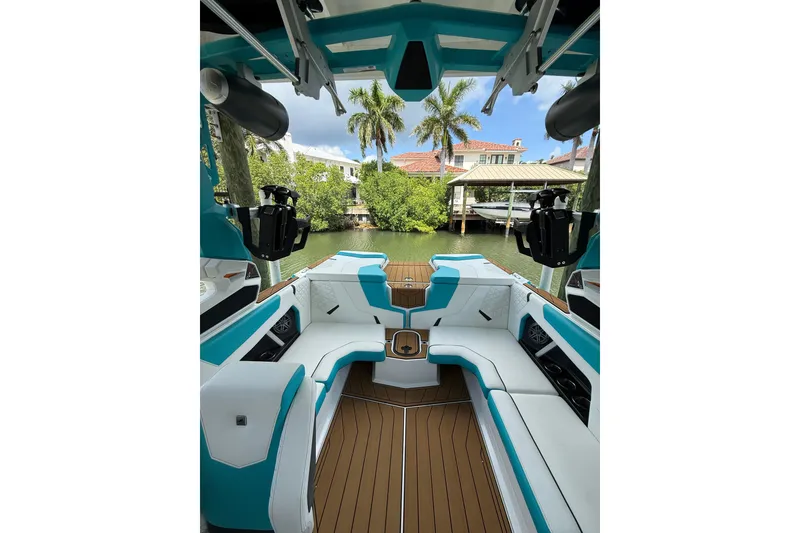 Slide: The Image of 2024 Nautique Super Air Nautique GS20 interior with teal and white seating, docked by lush greenery. - 4