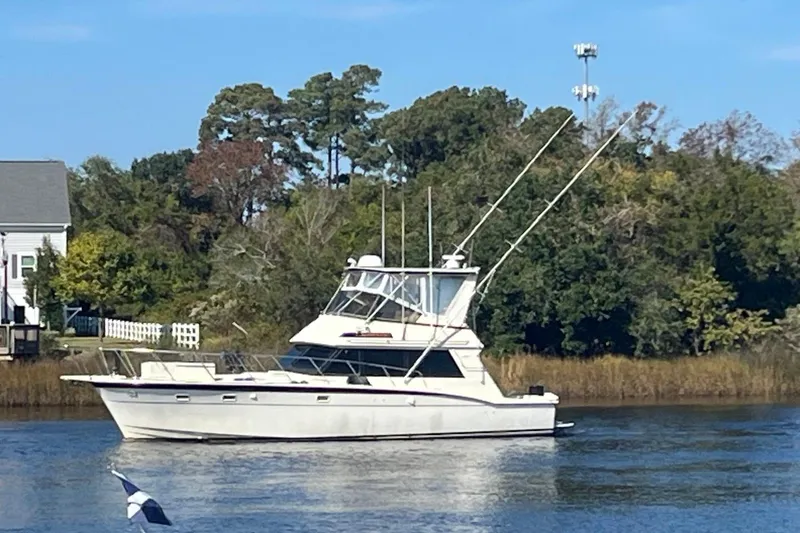 The Image of 1983 Hatteras 50 Convertible yacht on a serene river with lush greenery. - 1