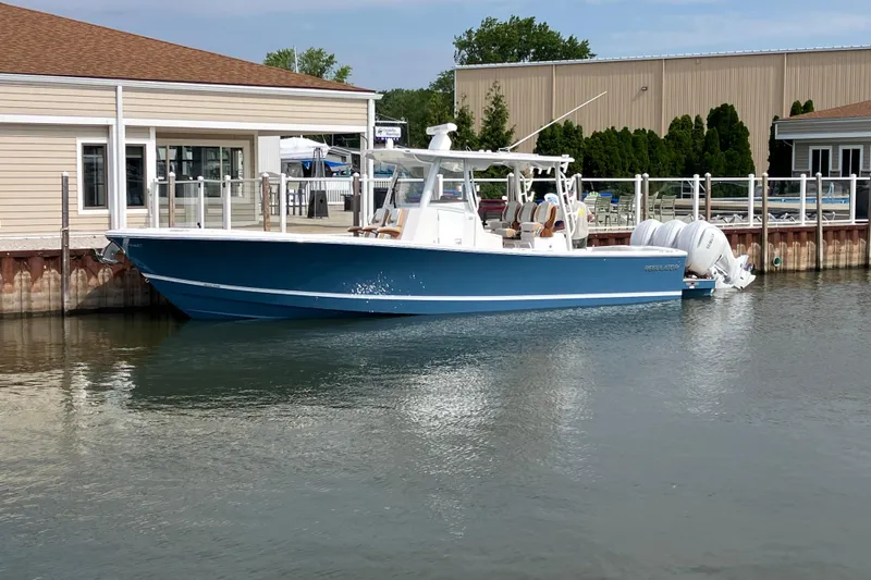 Slide: The Image of 2027 Regulator 35 boat docked by a waterfront building, featuring sleek blue design. - 2