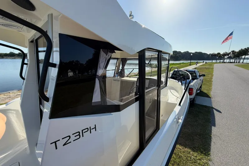 Slide: The Image of 2025 Bayliner Trophy T23 Pilothouse boat on trailer by a lakeside road. - 55