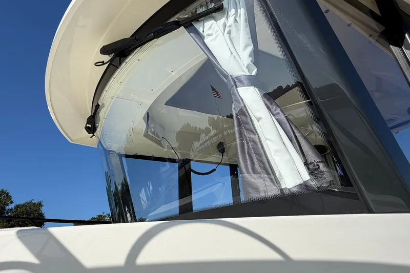 Slide: The Image of 2025 Bayliner Trophy T23 Pilothouse with sleek windows and curtains, under clear blue sky. - 10