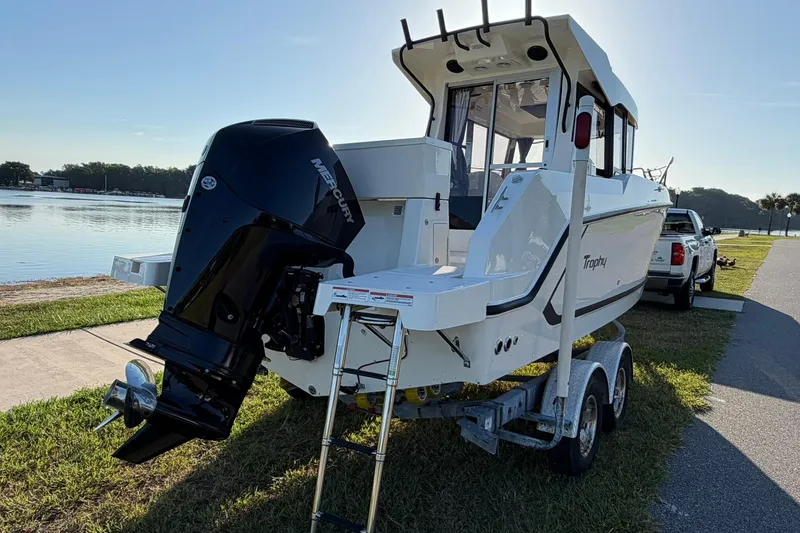 Slide: The Image of 2025 Bayliner Trophy T23 Pilothouse boat on trailer by a lakeside. - 59