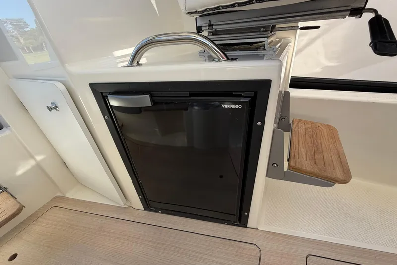 Slide: The Image of 2025 Bayliner Trophy T23 Pilothouse interior with compact fridge and wooden seat. - 19