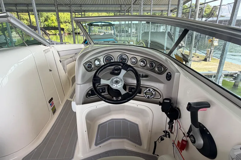 Slide: The Image of 2010 Bryant 255 boat dashboard with steering wheel and control panel in a marina setting. - 16