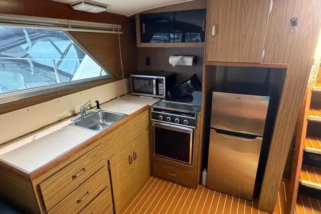 Slide: The Image of 1980 Chris-Craft 381 Catalina yacht kitchen with wood cabinetry, stove, microwave, and refrigerator. - 18