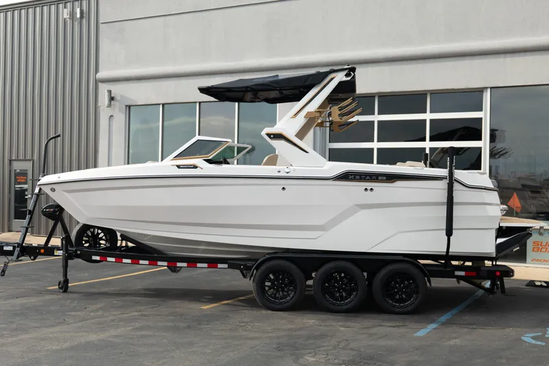 Slide: The Image of 2026 MasterCraft XStar 23 boat on trailer, parked outside a modern building. - 2